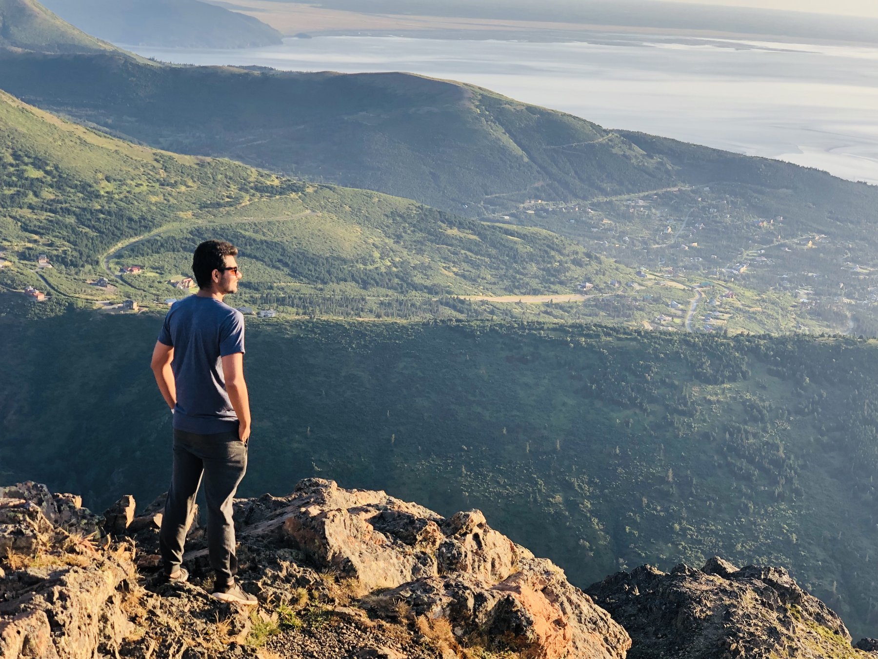 Anirudh standing on a rocky summit overlooking green valleys and the sea in Alaska